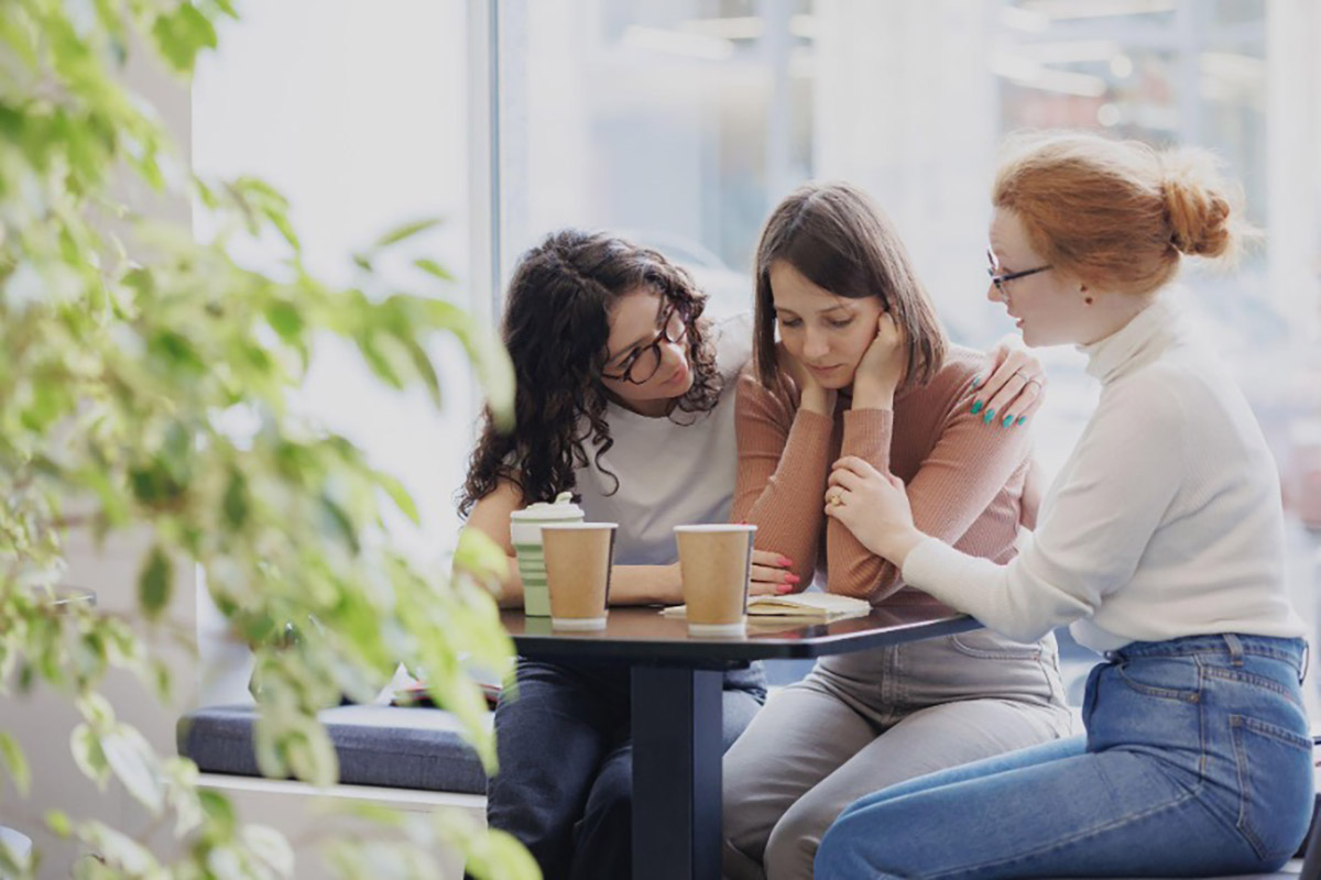Trois femmes assises dans un café qui réconfortent leur amie proche aidante